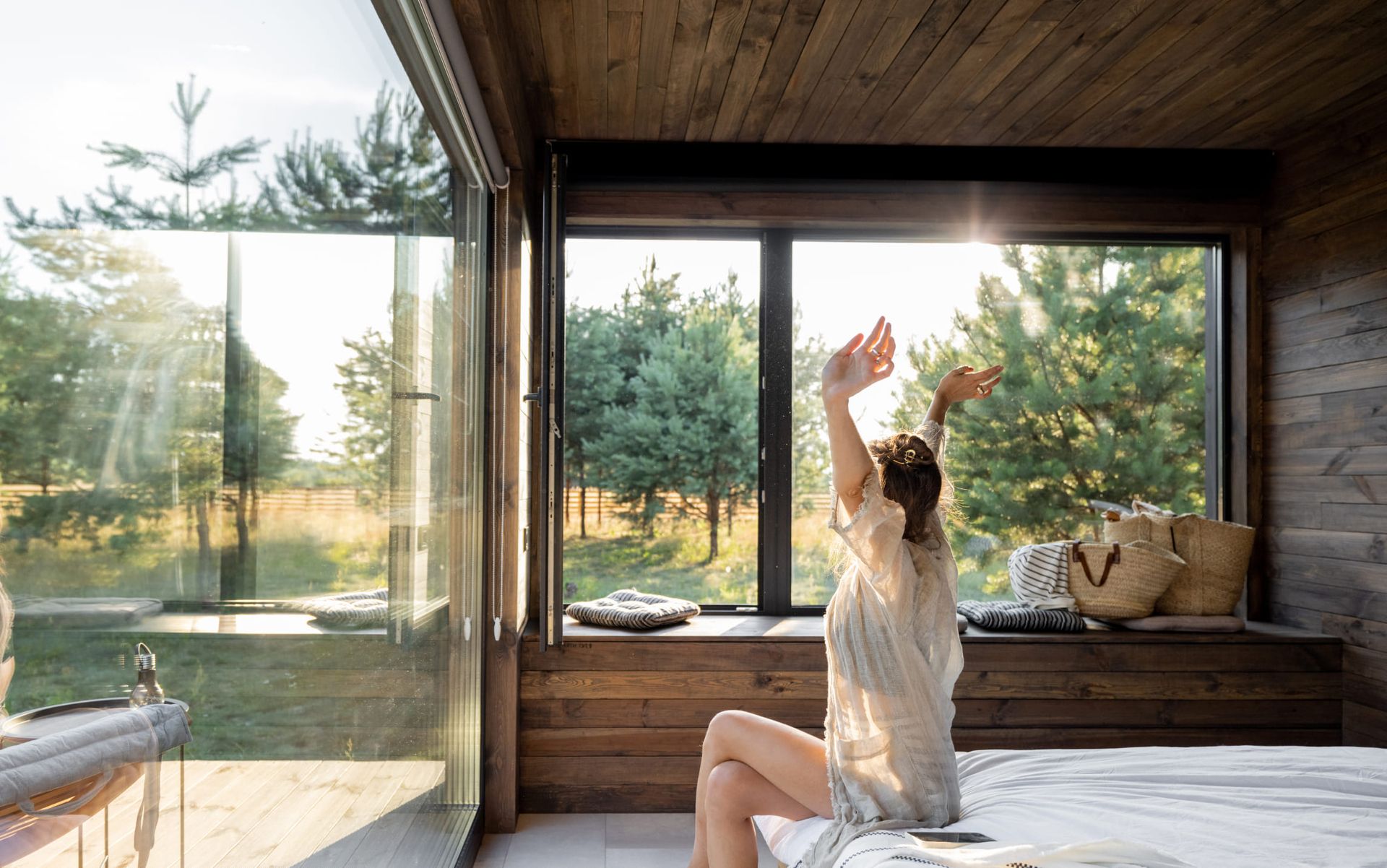 Eine Frau sitzt auf einem Bett in einem Zimmer mit großen Fensterfronten.